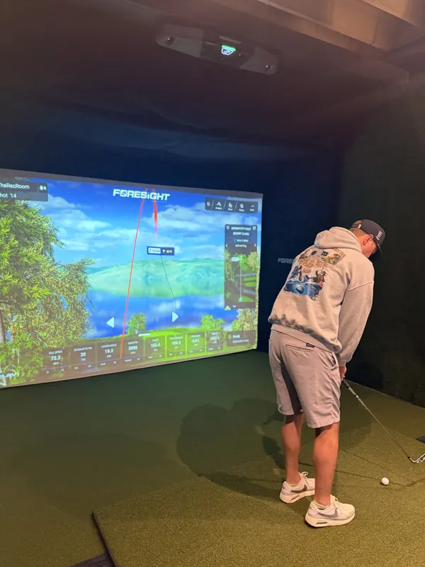 A golfer lines up a shot in a simulator bay, ball data on the big screen.