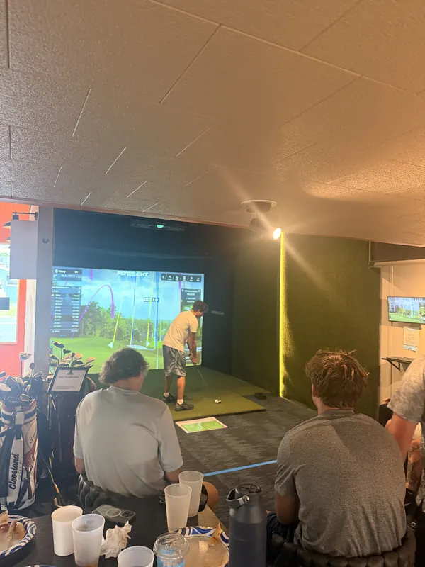 A golfer tees off while friends watch from the table.
